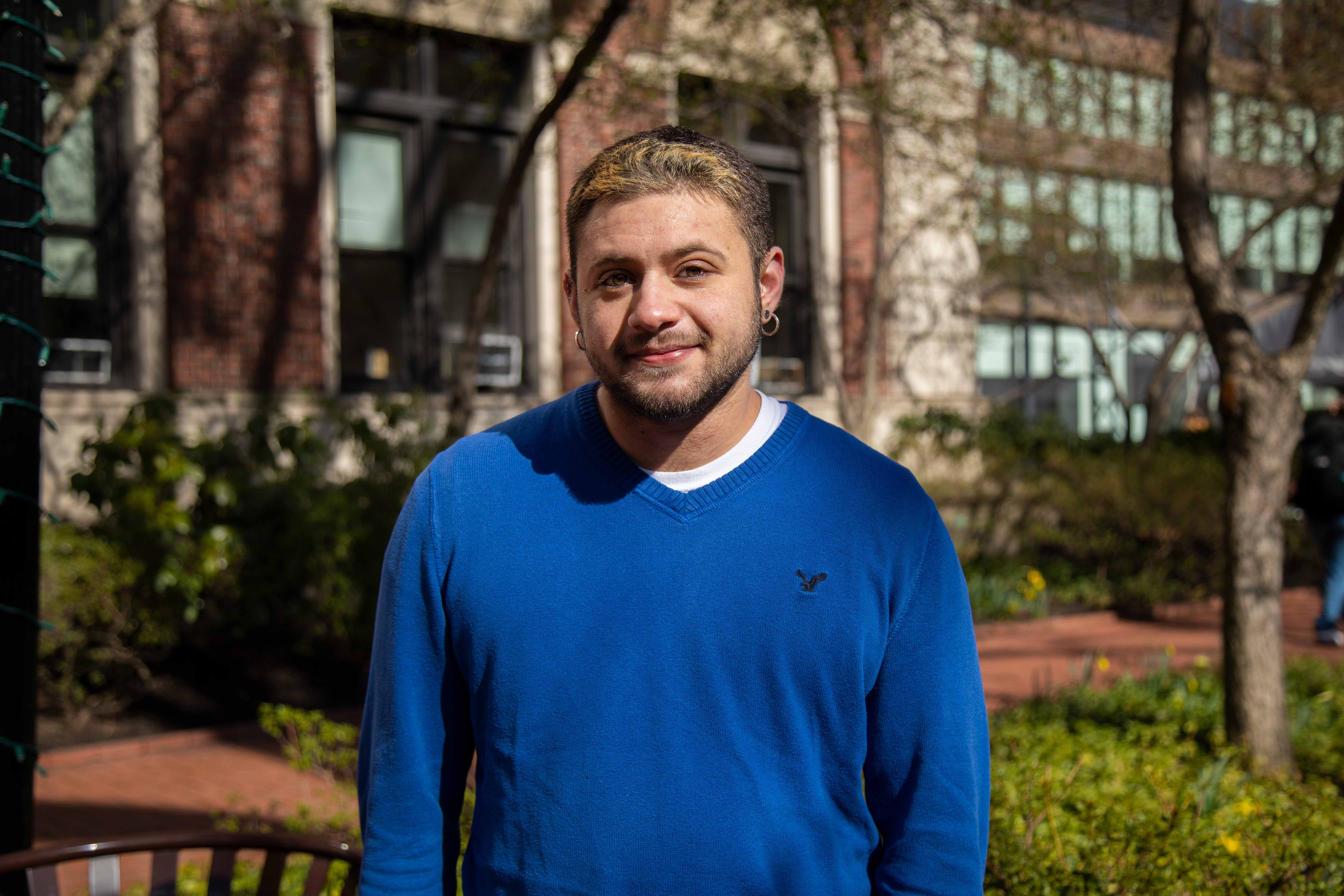 Dylan posing in front of Barnard Hall with a bright blue sweater on,